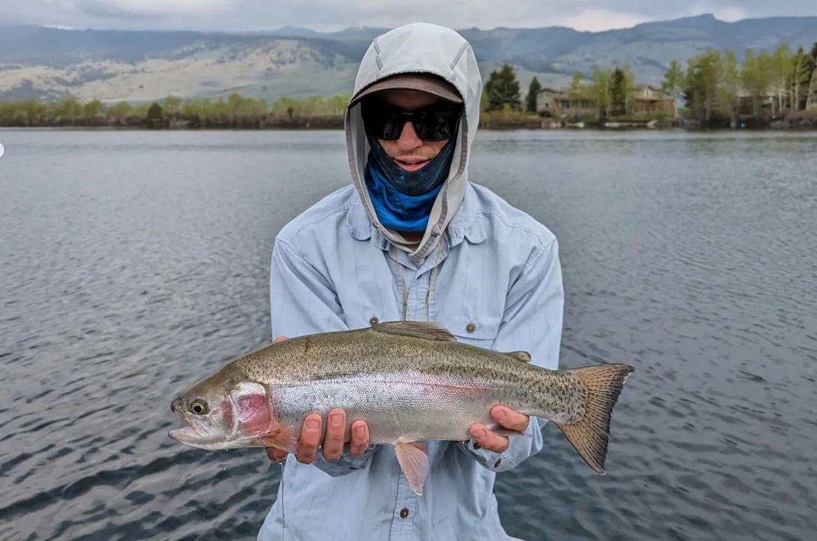 angler holding large rainbow trout with scenic lake in background