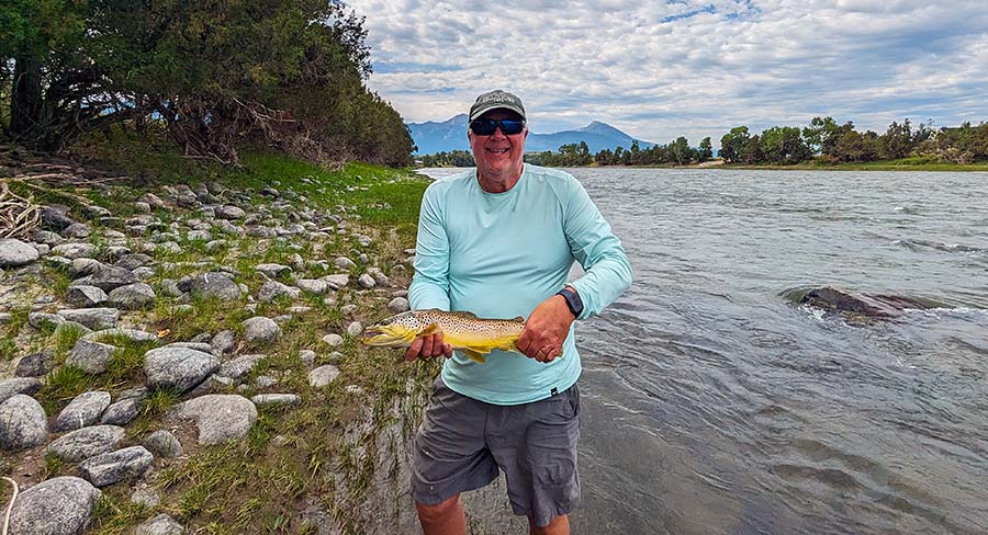 Angler with Yellowstone River brown trout. Image contains river, smiling fisherman, brown trout, trees