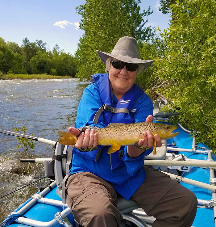 happy angler with brown trout in raft on a raging whitewater river