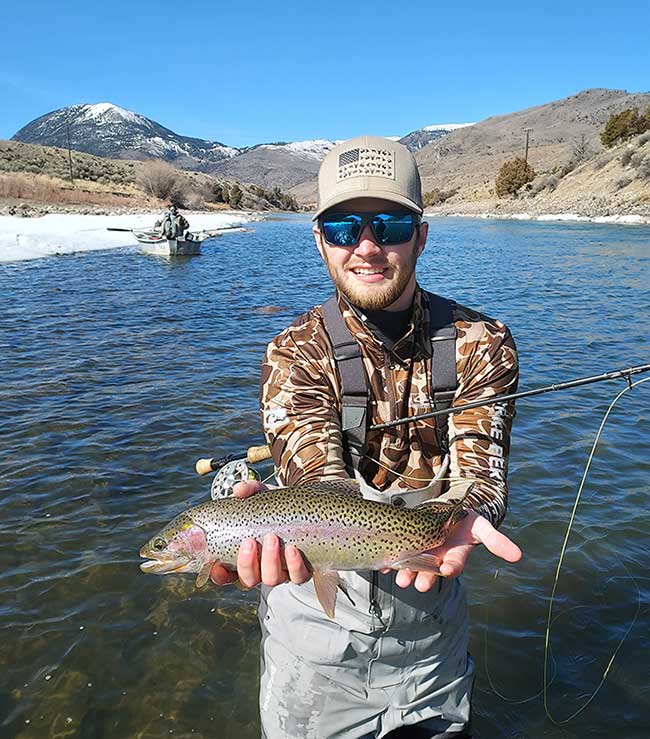 angler with nice early season rainbow trout. Snow and mountains in background.