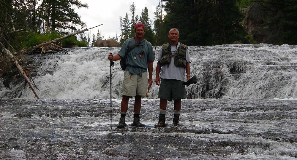 anglers standing midstream with waterfall in background