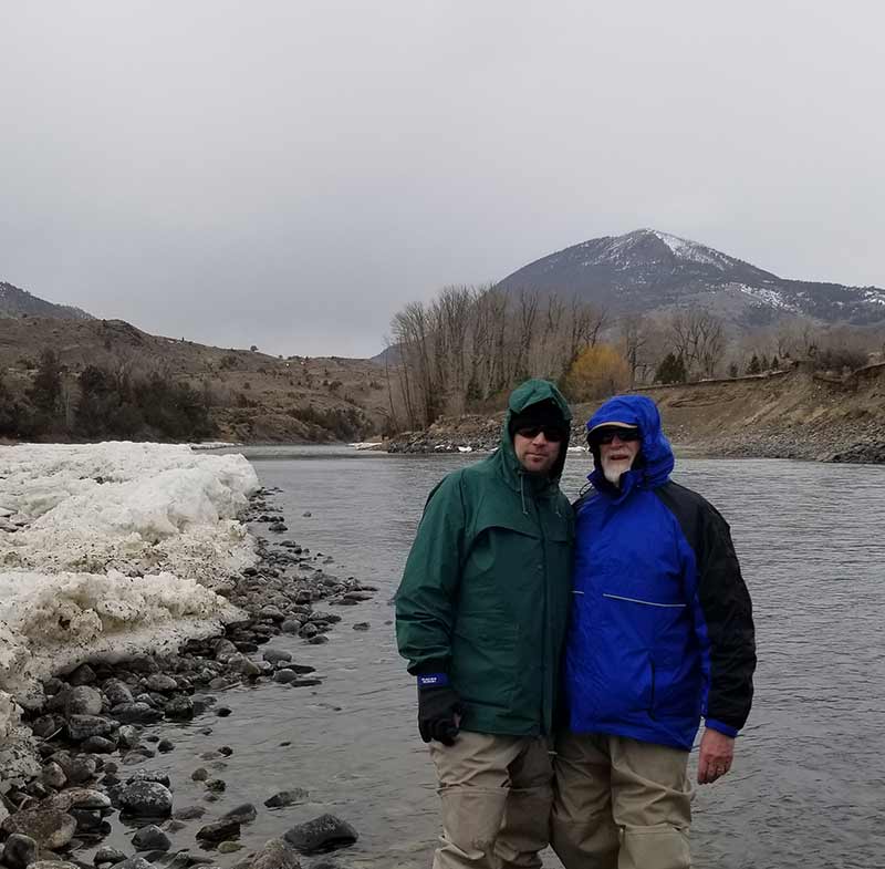 cold but happy anglers on icy yellowstone river. background shows gray skies, ice, river, and mountain