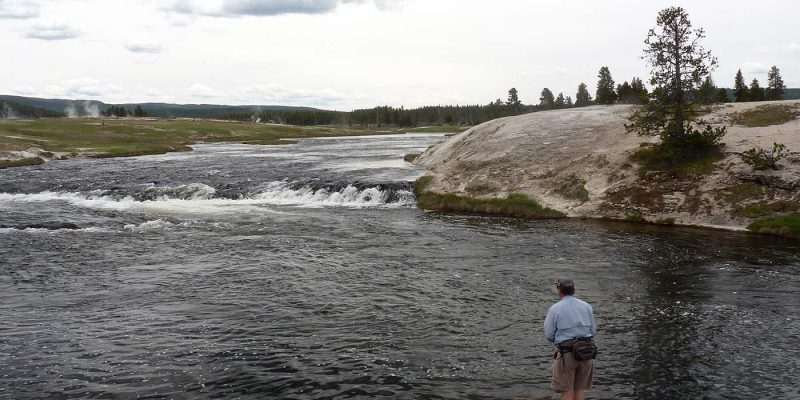 Angler fishing the Firehole River. Image contains fisherman, river, grass, and hot spring steam.