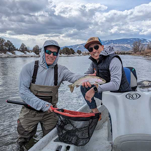 angler, guide, and trout, with wintery river scenery in background